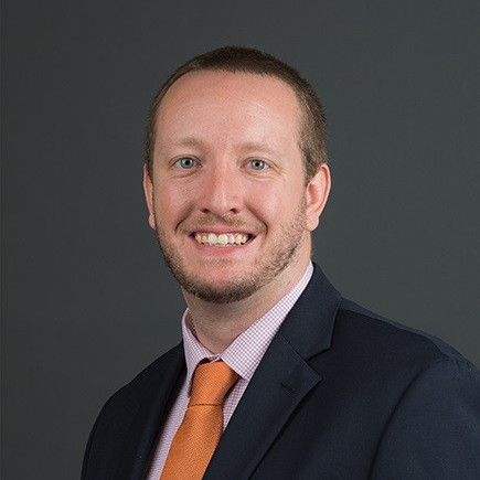 headshot of Aaron Bobik wearing an orange tie and black suit jacket